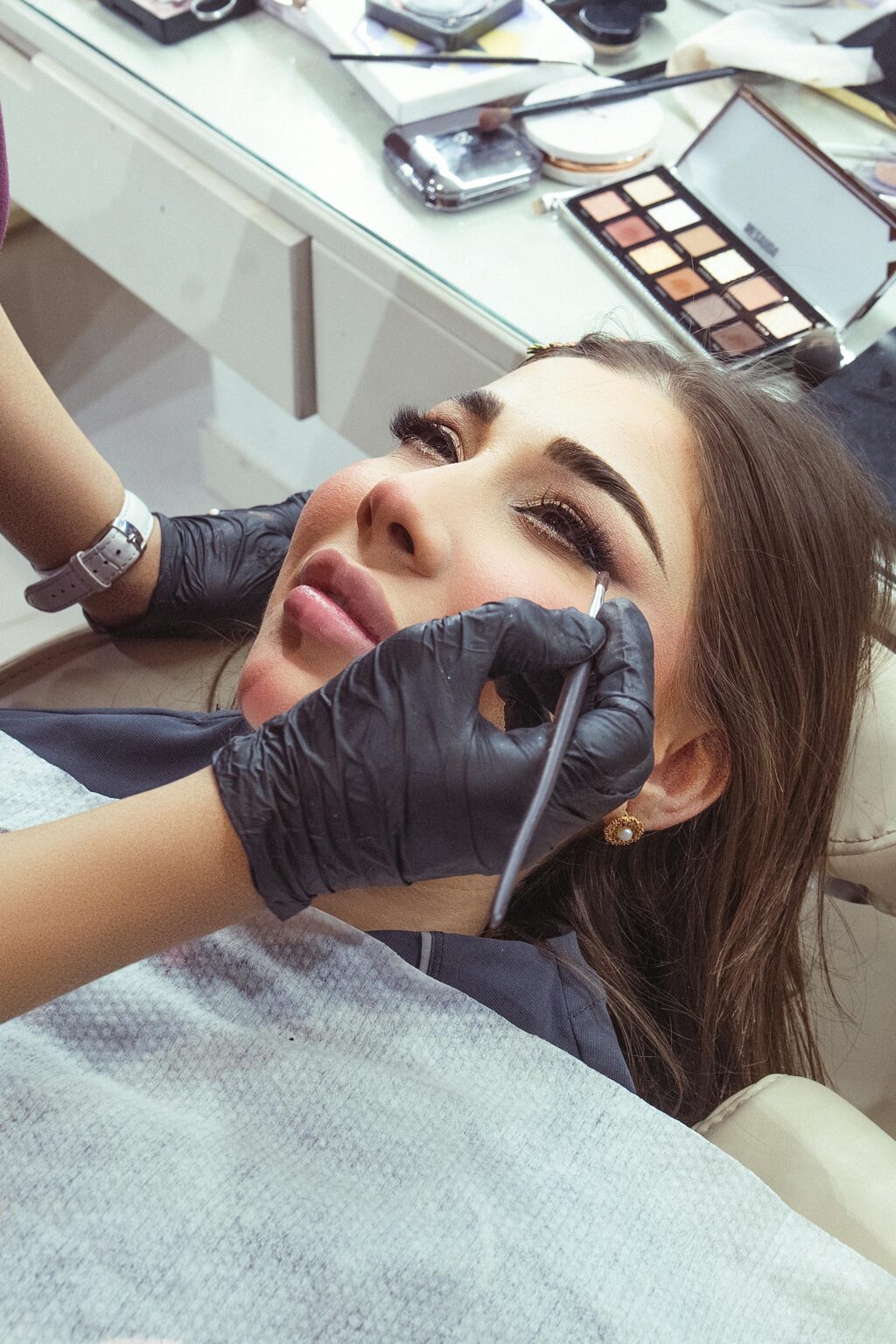 A professional makeup artist applying eye makeup to a woman at a salon.