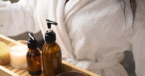 A woman in a bathrobe holds a tray of natural spa products, focusing on self-care.